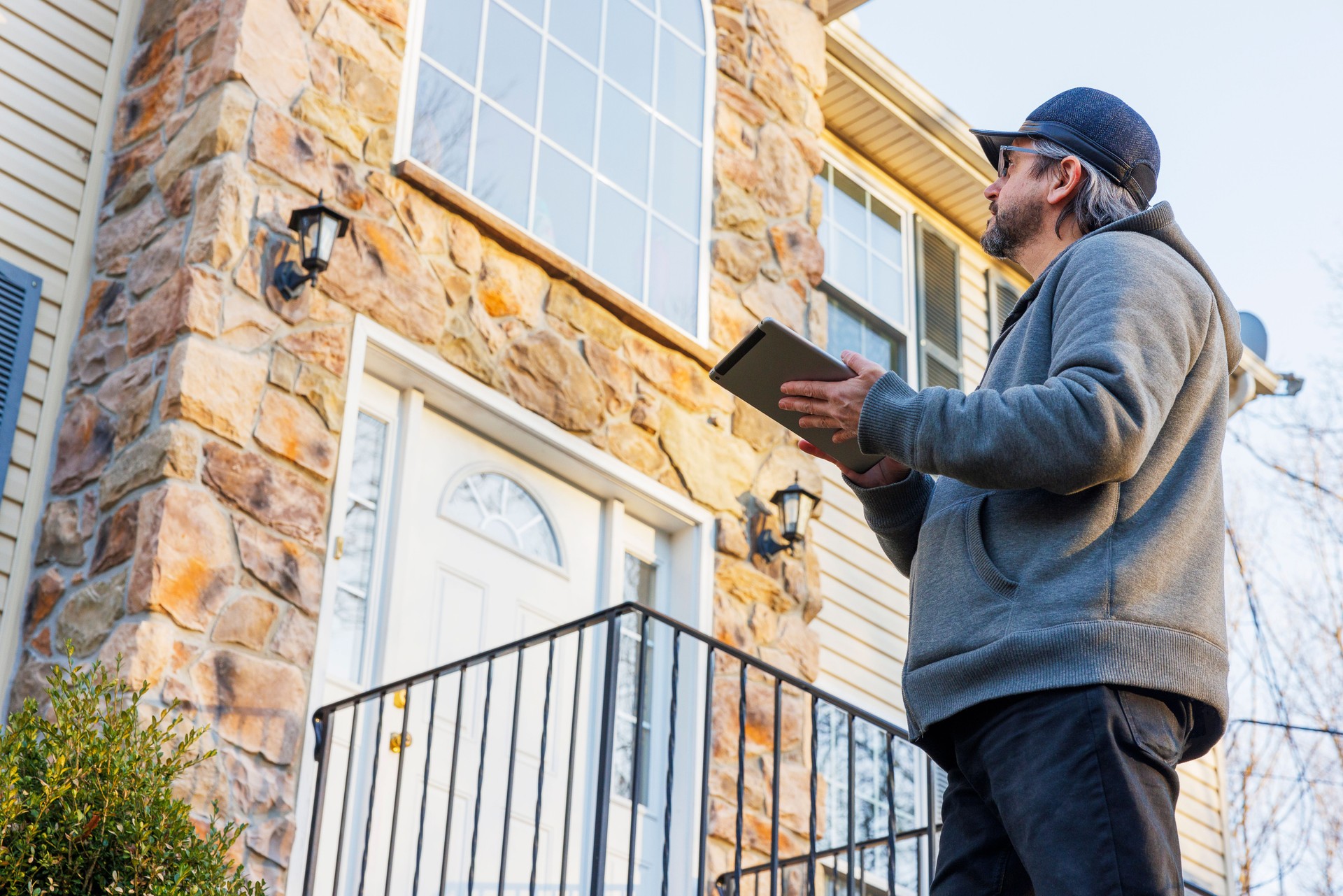 Mature house inspector, examining the house exterior from the front porch in Pennsylvania.