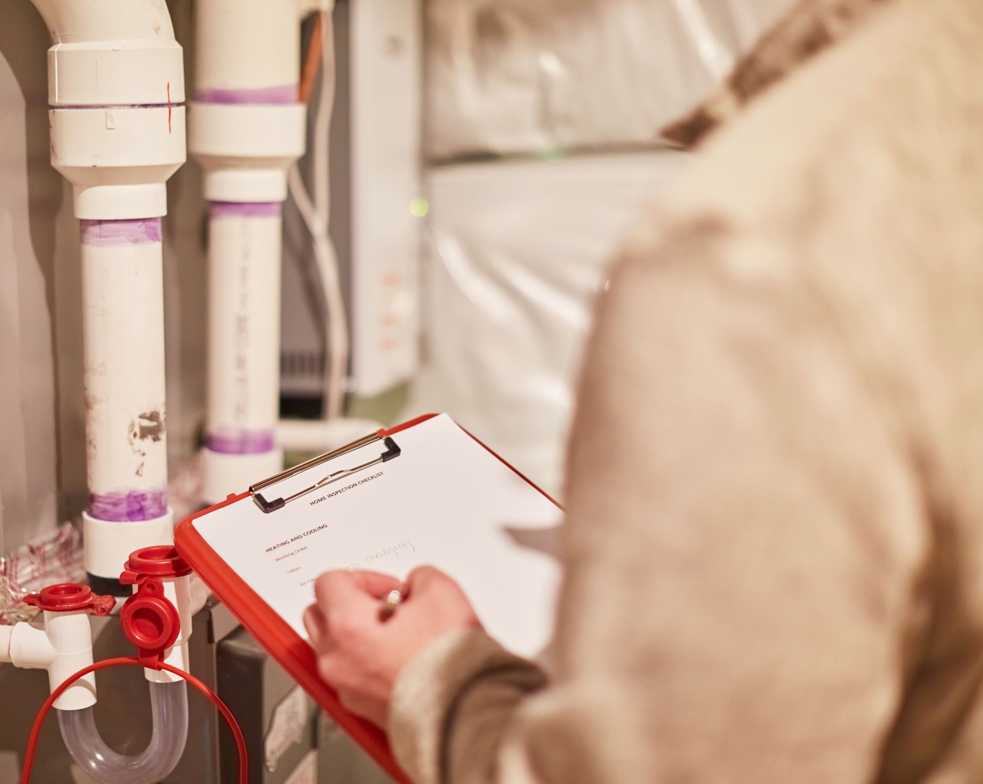 Male home inspector with clipboard assessing the heating system in the mechanical room of  a residential property